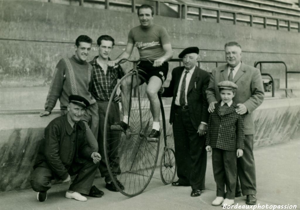 Marcel accroupi sourit de voir le champion cycliste Serge Lapébie sur un grand bi. À droite, le speaker des courses,  le directeur du stade  et le fils de Lapébie.